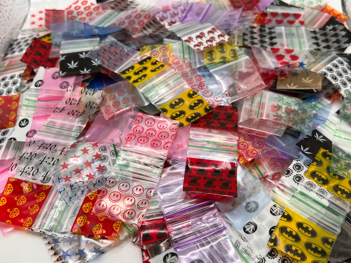 A pile of small clear and printed plastic zip bags with various printed designs including smiley faces, stars, Batman logos, leaf. zip  poly baggies