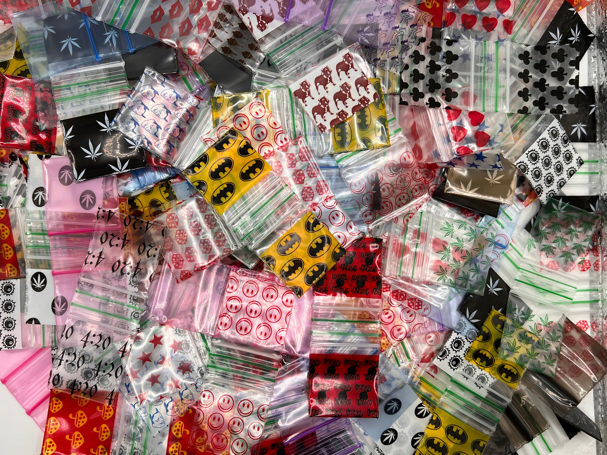 A dense pile of small clear and printed plastic zip baggies filled with colorful printed patterns, including leafs, hearts, skulls, stars, and text, photographed from above.
