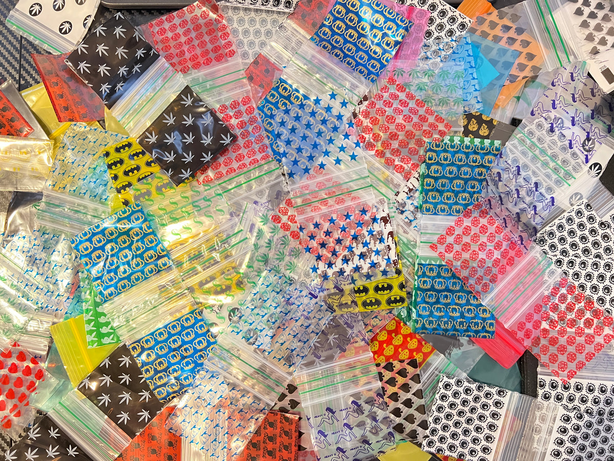 Overhead view of assorted 50x50mm (2x2 inch) printed poly baggies and resealable plastic zip bags in a variety of designs.